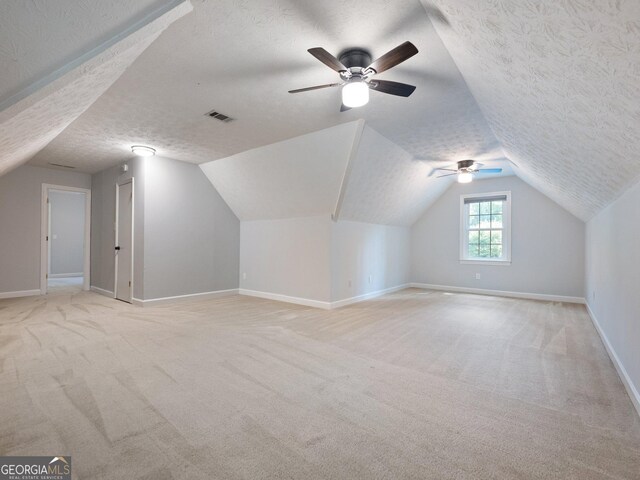 additional living space featuring ceiling fan, a textured ceiling, light carpet, and vaulted ceiling