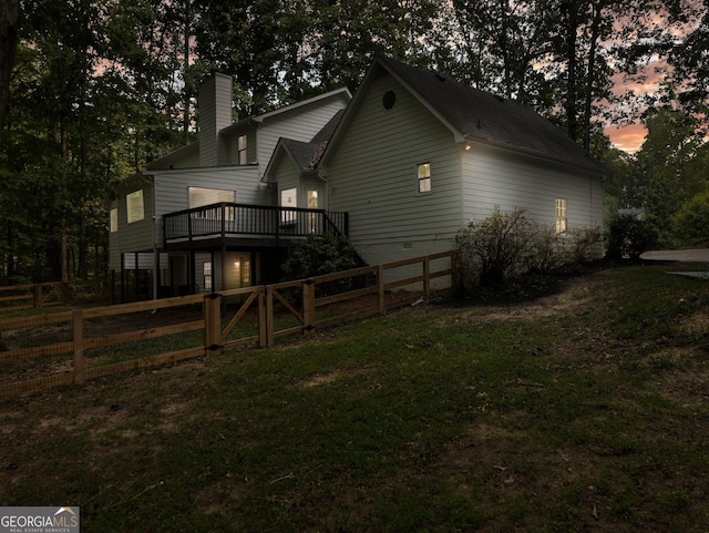 property exterior at dusk featuring a lawn and a deck