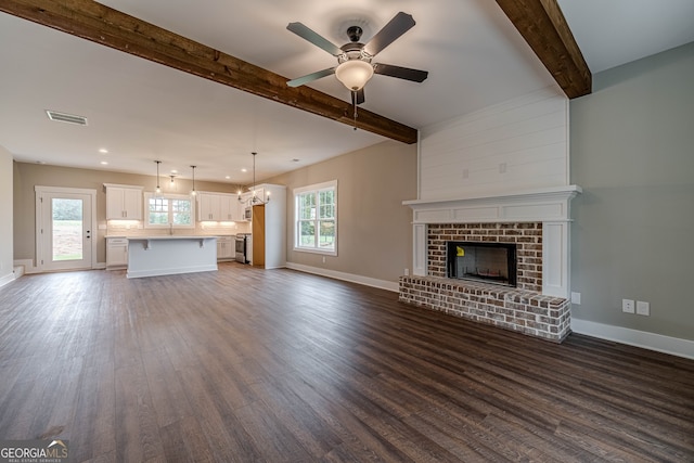 unfurnished living room with a brick fireplace, ceiling fan with notable chandelier, dark hardwood / wood-style flooring, and a wealth of natural light