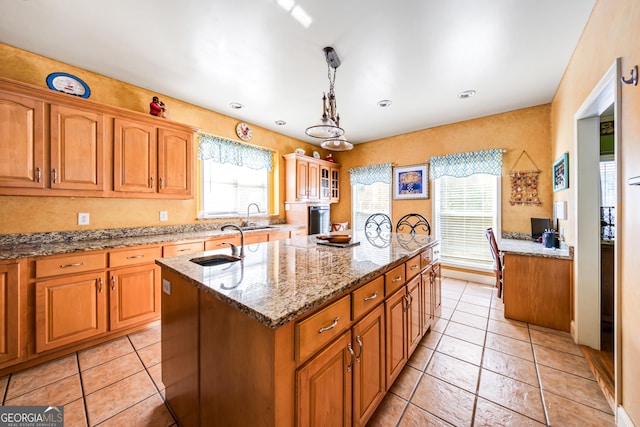 kitchen with a wealth of natural light, a center island with sink, pendant lighting, and light tile patterned flooring