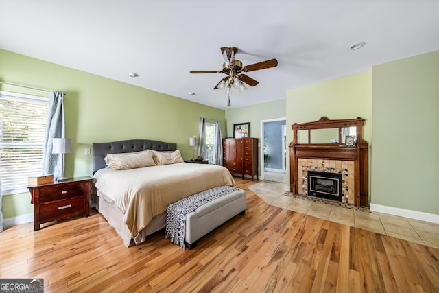 bedroom featuring a tiled fireplace, multiple windows, light hardwood / wood-style flooring, and ceiling fan