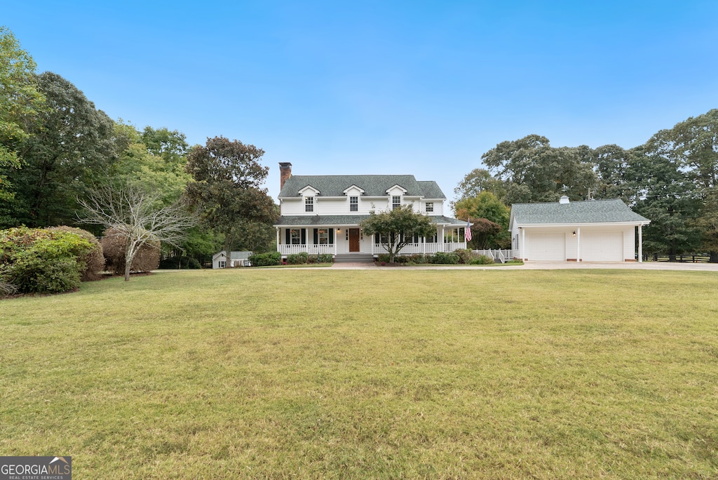 new england style home with a front lawn, covered porch, and a garage