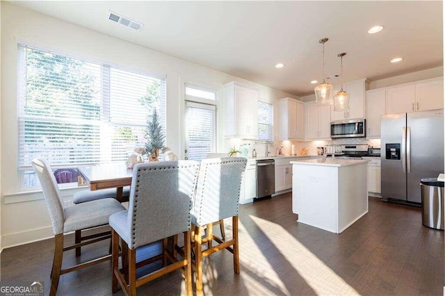 kitchen featuring stainless steel appliances, white cabinets, a center island, and decorative light fixtures