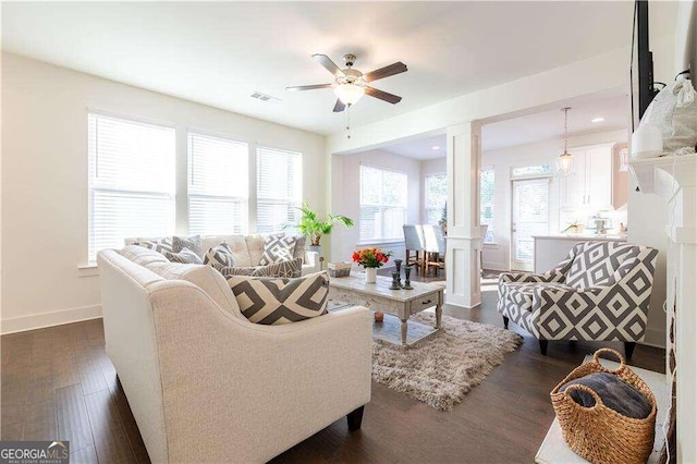 living room featuring decorative columns, ceiling fan, and dark wood-type flooring