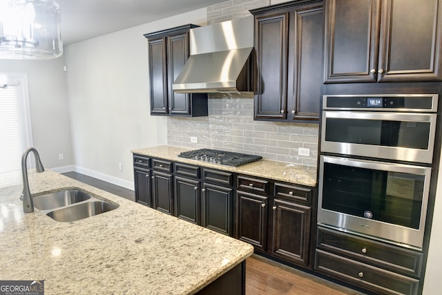 kitchen with light stone counters, sink, wall chimney exhaust hood, stainless steel appliances, and decorative backsplash