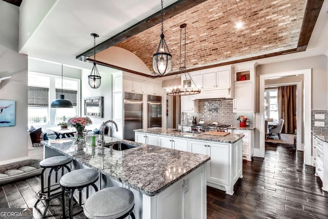 kitchen featuring a large island, pendant lighting, sink, white cabinetry, and brick ceiling