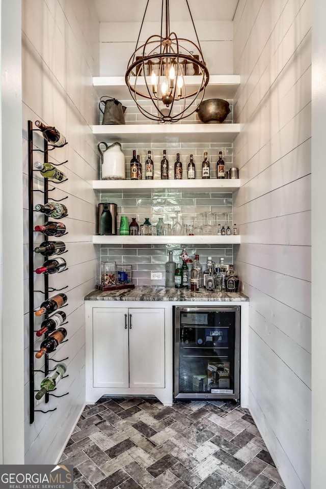 bar with pendant lighting, dark stone counters, beverage cooler, white cabinets, and an inviting chandelier