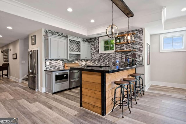 kitchen with light hardwood / wood-style floors, a kitchen bar, gray cabinetry, decorative backsplash, and appliances with stainless steel finishes