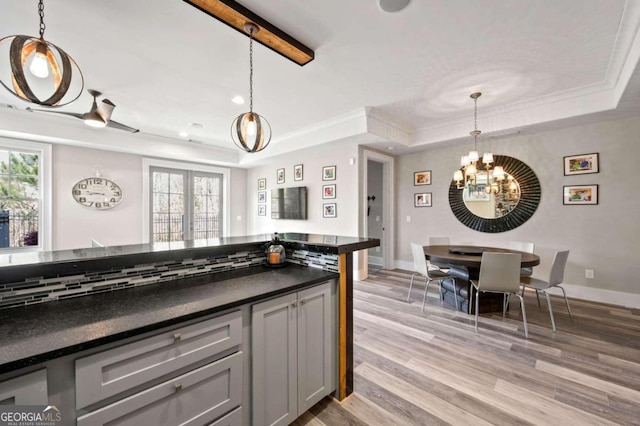 kitchen with hanging light fixtures, a raised ceiling, light hardwood / wood-style floors, and plenty of natural light