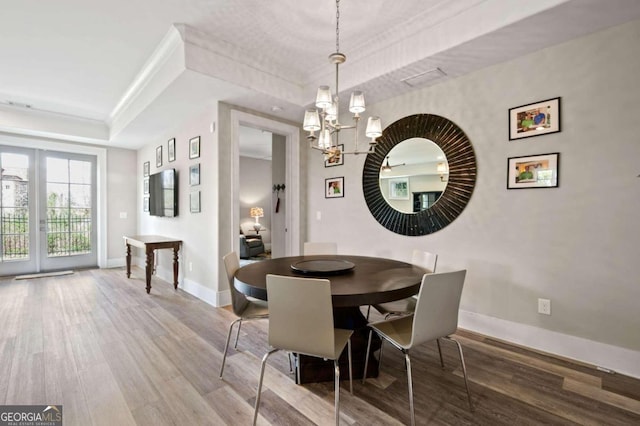 dining space featuring wood-type flooring, an inviting chandelier, and a raised ceiling