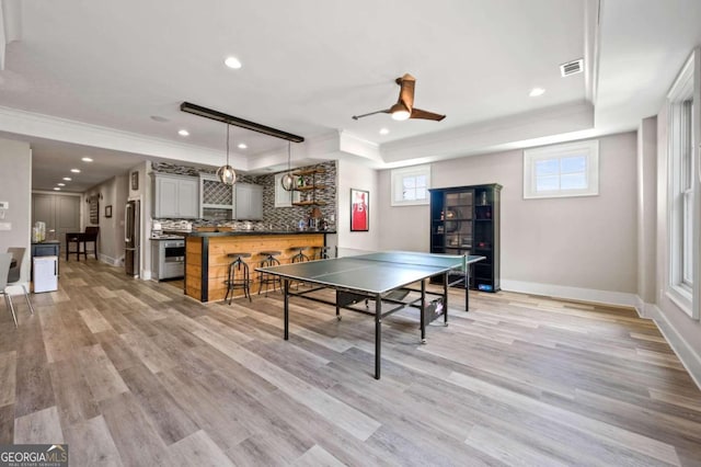 playroom featuring light wood-type flooring, a raised ceiling, ornamental molding, and ceiling fan