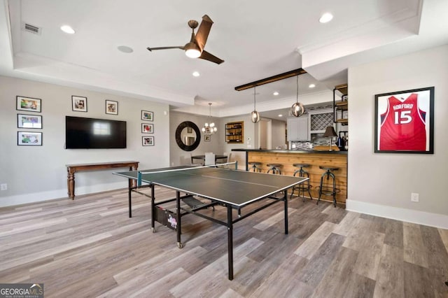 playroom with bar area, light hardwood / wood-style floors, a tray ceiling, and ceiling fan