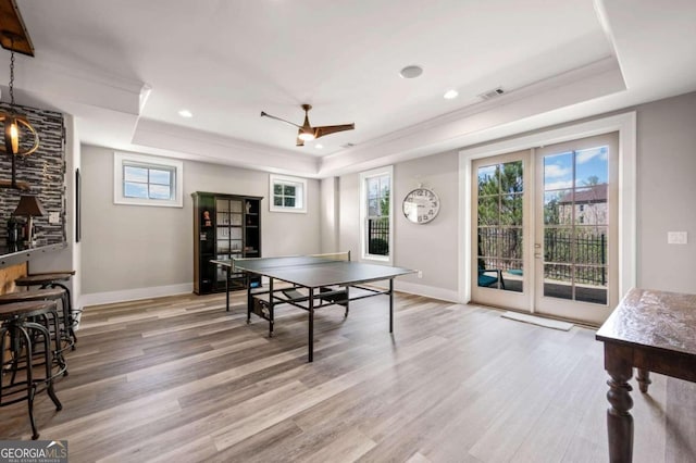 rec room with light wood-type flooring, a tray ceiling, and a healthy amount of sunlight