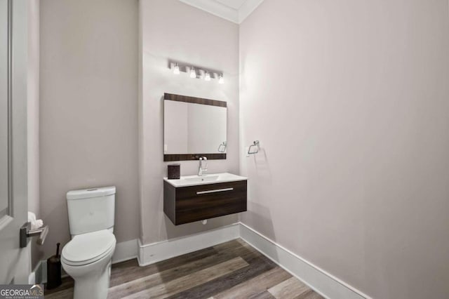 bathroom featuring wood-type flooring, vanity, crown molding, and toilet