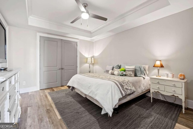 bedroom featuring a closet, light wood-type flooring, a tray ceiling, and ceiling fan