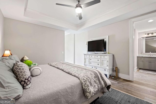 bedroom featuring ceiling fan, a raised ceiling, sink, light wood-type flooring, and ensuite bath