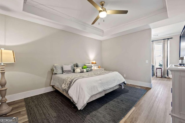 bedroom with wood-type flooring, a tray ceiling, and ceiling fan