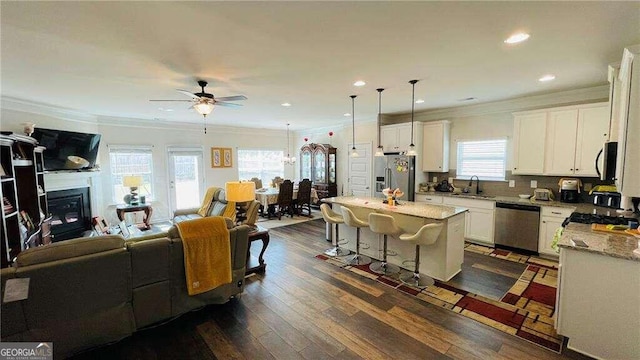 kitchen with ceiling fan with notable chandelier, a kitchen island, light stone countertops, stainless steel appliances, and decorative light fixtures