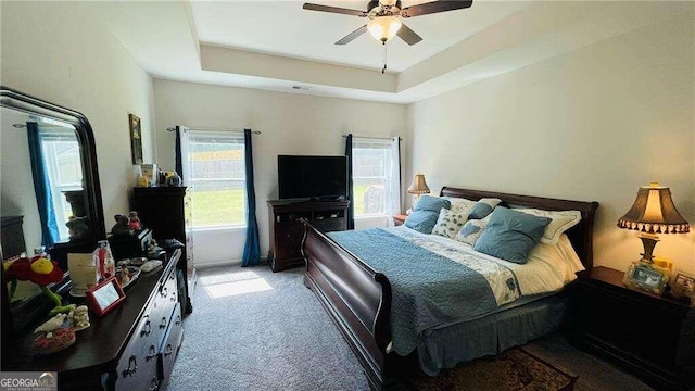 carpeted bedroom featuring ceiling fan and a raised ceiling