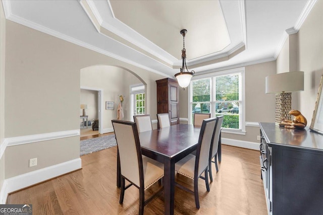 dining space with a raised ceiling, crown molding, and light hardwood / wood-style flooring