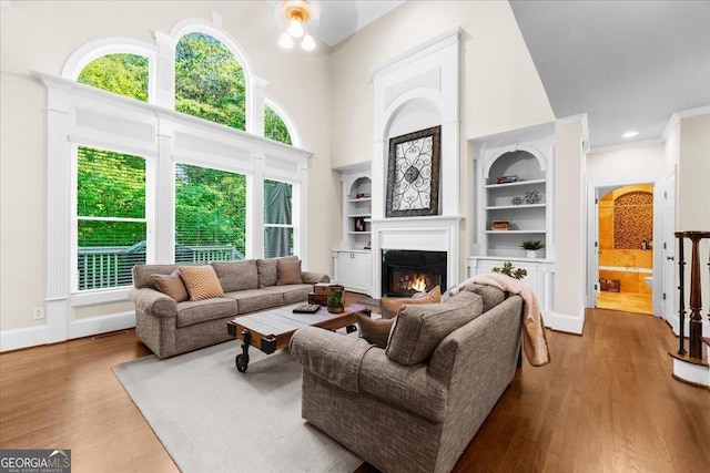 living room featuring crown molding, built in features, light hardwood / wood-style floors, and a high ceiling