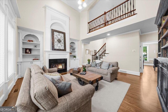 living room with hardwood / wood-style flooring, built in shelves, and a towering ceiling