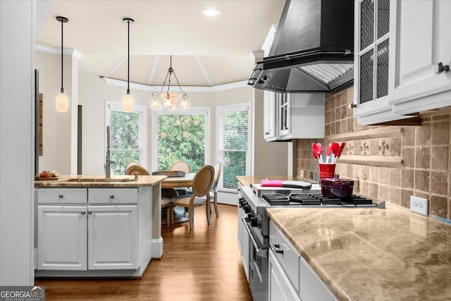 kitchen featuring white cabinetry, ventilation hood, backsplash, decorative light fixtures, and high end stainless steel range