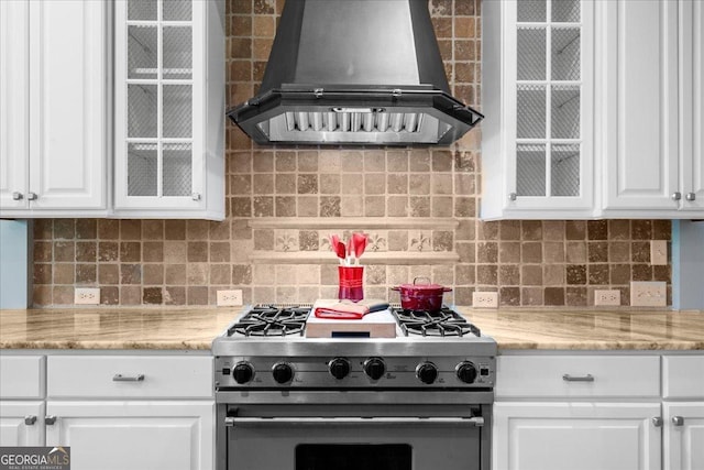 kitchen with white cabinets, decorative backsplash, high end stainless steel range oven, and exhaust hood