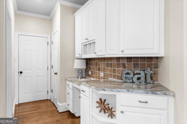 kitchen featuring light stone countertops, backsplash, crown molding, white cabinets, and light wood-type flooring