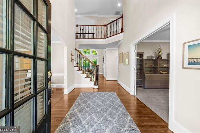 entryway with dark hardwood / wood-style flooring, a towering ceiling, and crown molding