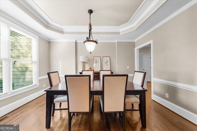 dining space featuring hardwood / wood-style flooring, a raised ceiling, and ornamental molding