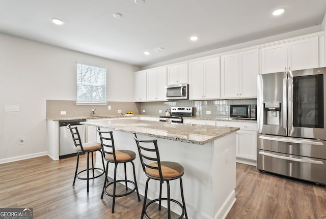 kitchen featuring white cabinets, dark wood-type flooring, stainless steel appliances, a center island, and light stone countertops