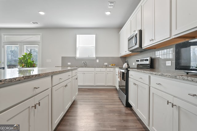 kitchen with light stone counters, white cabinets, backsplash, dark wood-type flooring, and stainless steel appliances