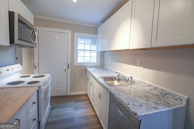 kitchen with appliances with stainless steel finishes, ornamental molding, sink, white cabinetry, and butcher block counters