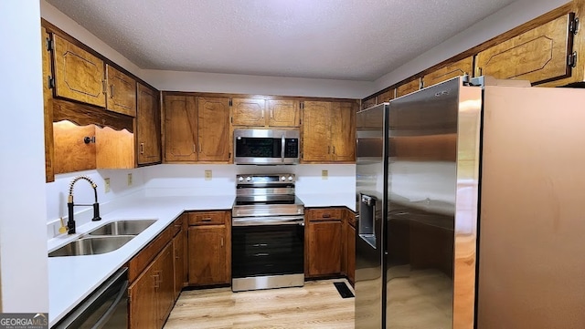 kitchen featuring light hardwood / wood-style floors, a textured ceiling, stainless steel appliances, and sink