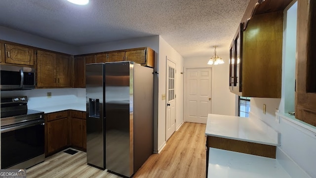 kitchen with pendant lighting, stainless steel appliances, light wood-type flooring, a textured ceiling, and a notable chandelier