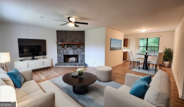 living room featuring light hardwood / wood-style floors, a stone fireplace, and ceiling fan