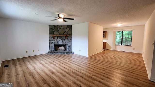 unfurnished living room with a textured ceiling, light hardwood / wood-style floors, ceiling fan, and a stone fireplace