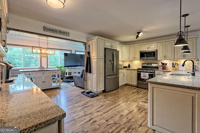 kitchen featuring light wood-type flooring, hanging light fixtures, sink, appliances with stainless steel finishes, and light stone countertops