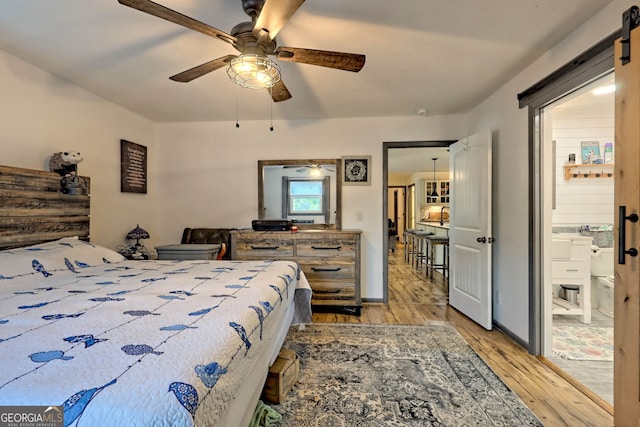 bedroom featuring light wood-type flooring, ceiling fan, and a barn door