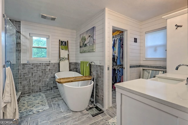 bathroom featuring independent shower and bath, vanity, and wood walls