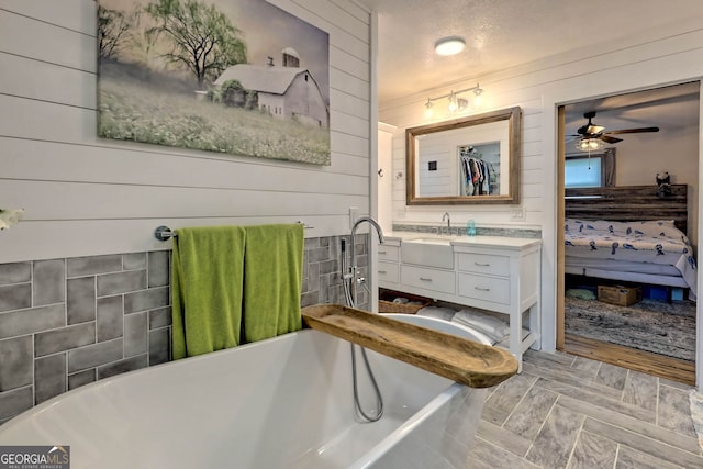 bathroom with ceiling fan, vanity, a tub, wood-type flooring, and a textured ceiling