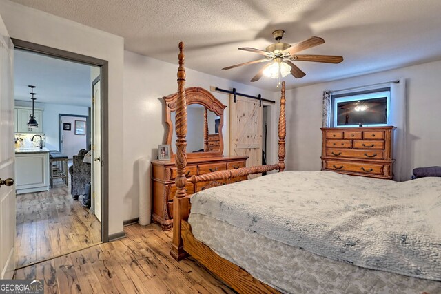 bedroom with ceiling fan, a textured ceiling, light wood-type flooring, and a barn door