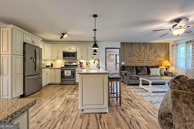 kitchen with light stone countertops, cream cabinets, decorative light fixtures, stainless steel appliances, and light wood-type flooring