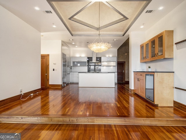 kitchen with wall chimney exhaust hood, dark wood-type flooring, hanging light fixtures, a chandelier, and fridge