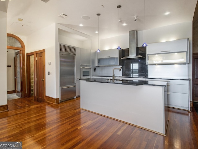 kitchen featuring a kitchen island with sink, sink, wall chimney exhaust hood, and stainless steel built in refrigerator