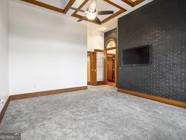 carpeted empty room with high vaulted ceiling, ceiling fan, and brick wall