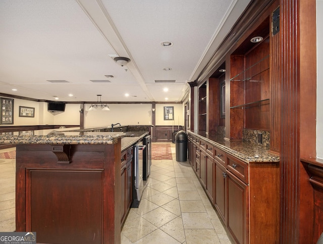 kitchen featuring a large island with sink, ornamental molding, and dark stone countertops