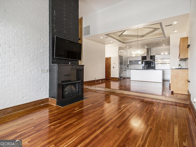 unfurnished living room featuring sink, a tray ceiling, dark hardwood / wood-style flooring, brick wall, and a chandelier