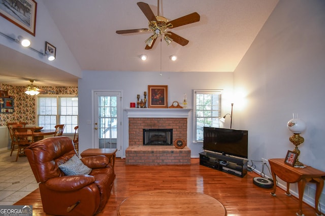 living room with ceiling fan, light wood-type flooring, a brick fireplace, and high vaulted ceiling